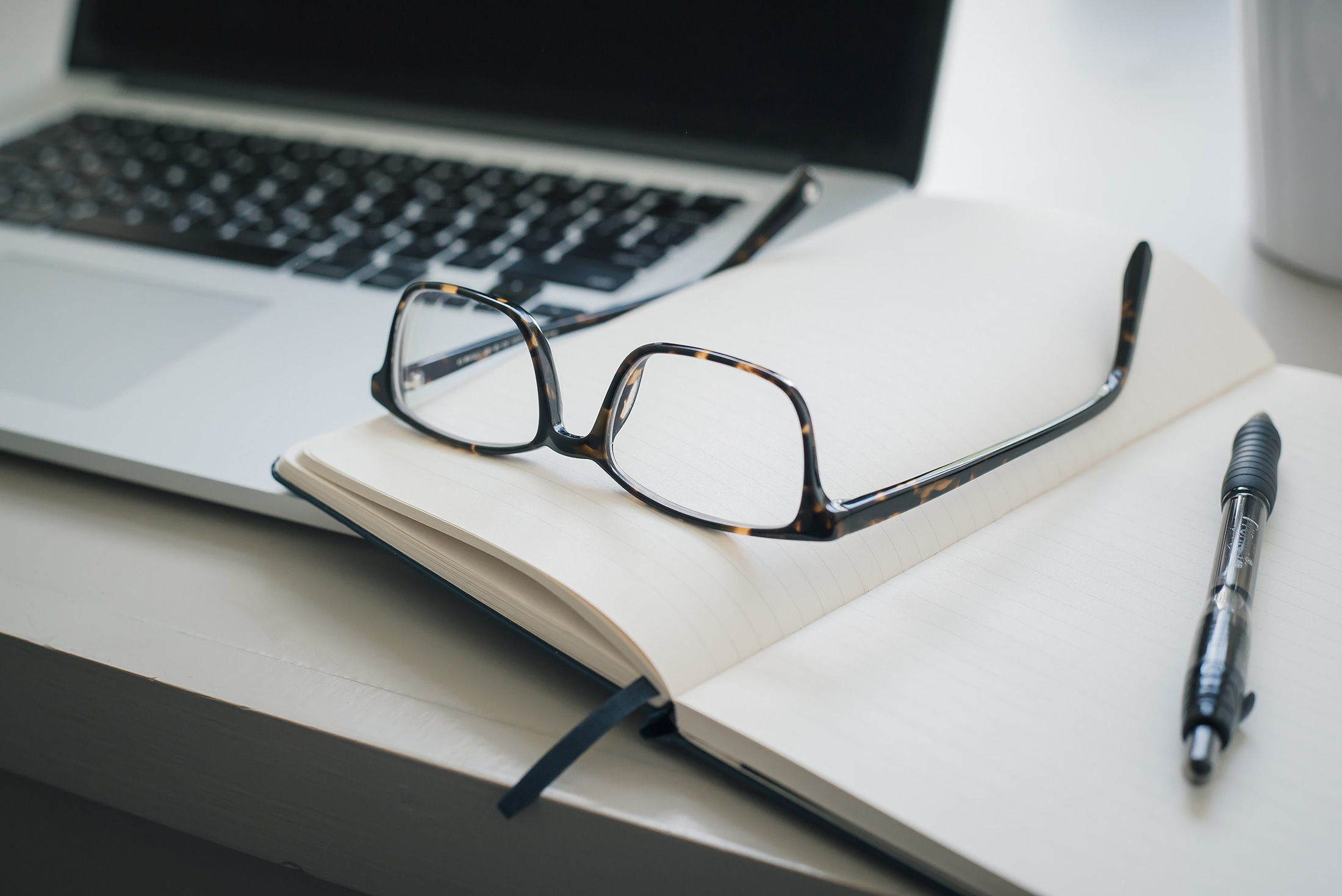 glasses sitting on a notepad next to a laptop