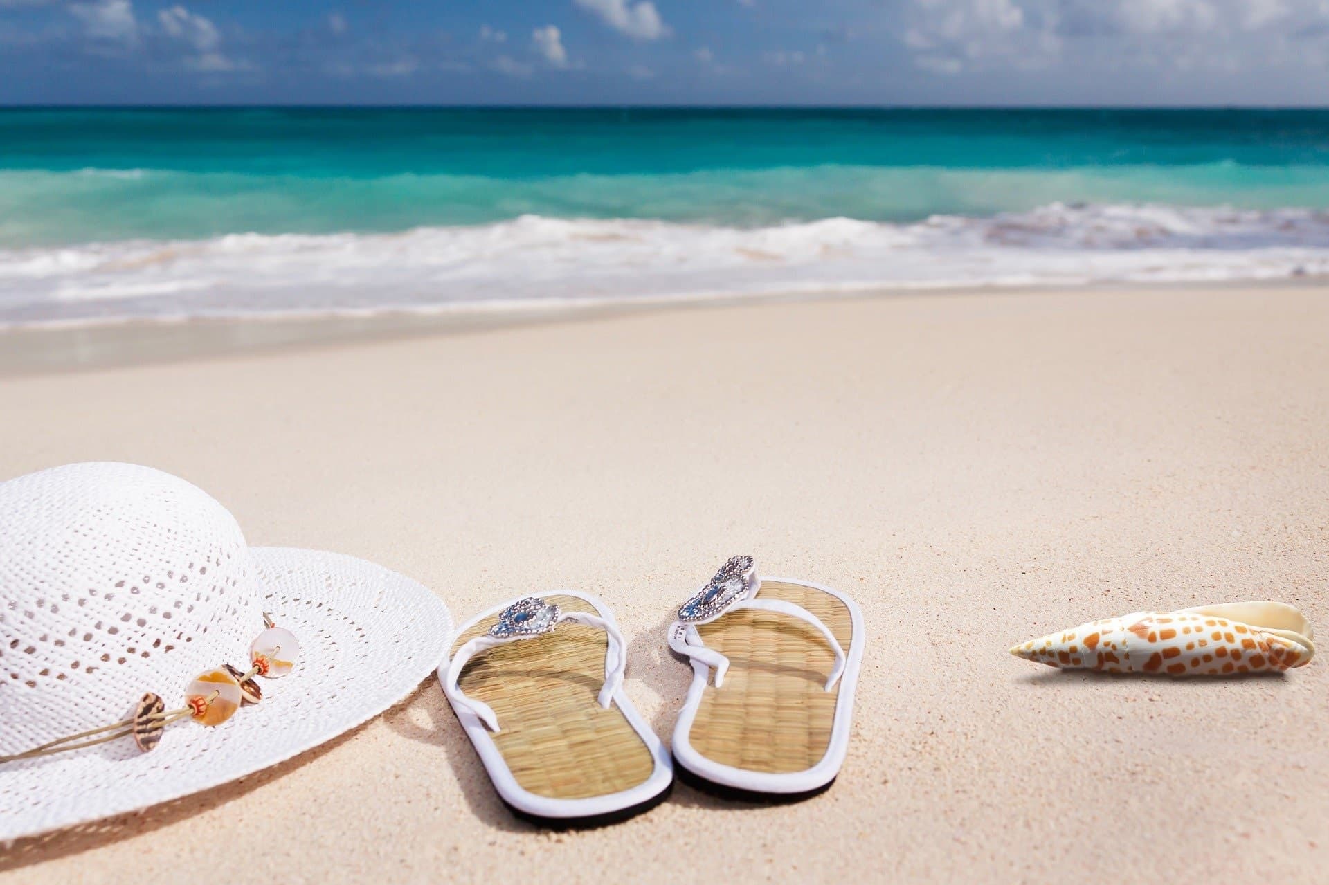 sandals, a sunhat, and a shell on a beach
