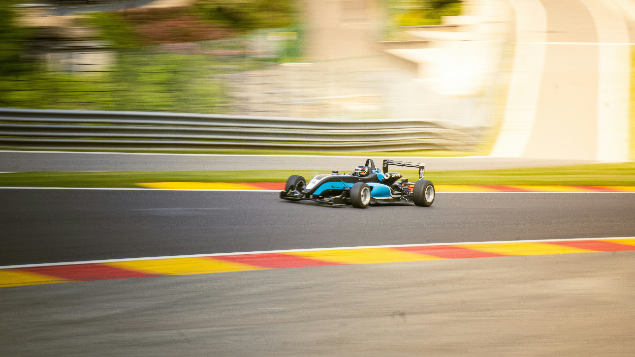 A formula 1 car alone on a race track. The bckground is blurred, indicting that the car is moving very quickly and is ahead of the other cars.
