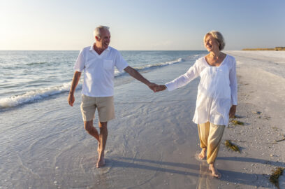 Older man and woman holding hands walking on a beach together
