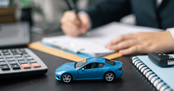 Blue toy car on a desk and a man completing paperworlk.