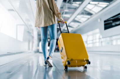 Woman walking in an airport terminal and pulling her suitcase behind her.