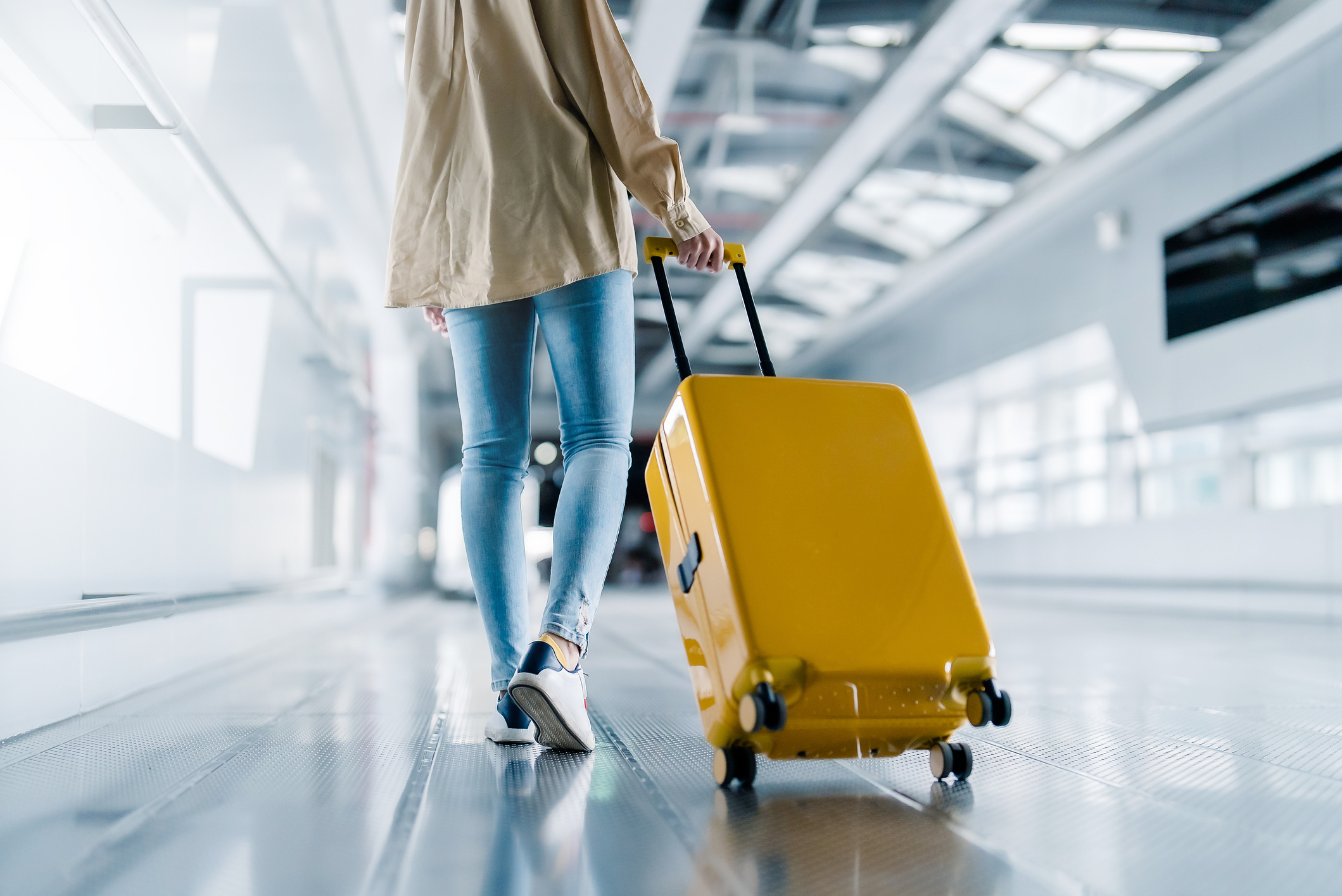 Woman walking in an airport terminal and pulling her suitcase behind her.
