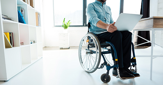Man sitting in wheel chair with laptop, home office setting