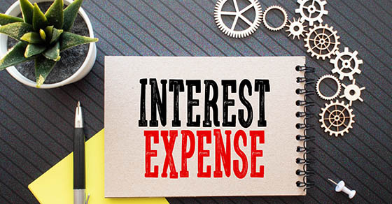 Business concept. Text Interest Expense with banknote, pen and calculator on wooden table background.