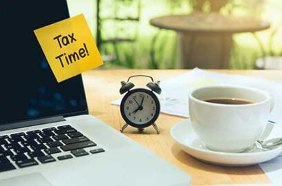 Laptop on desk, alarm clock, coffee cup, sticky note, Text: Tax Time,