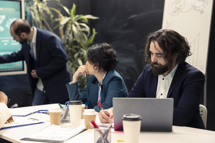Business colleagues in a meeting, sitting around a conference table with laptops, pens, cups of coffee