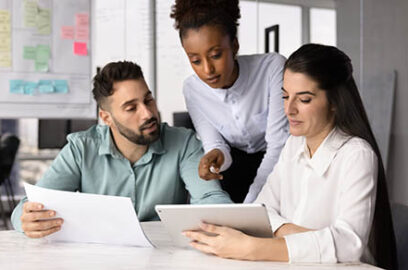 Three,Colleagues,Gathered,Around,Conference,Table,,Looking,At,Tablet,,Hold