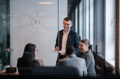 Team of four people in a modern office building, sitting around conference table in front of a whiteboard