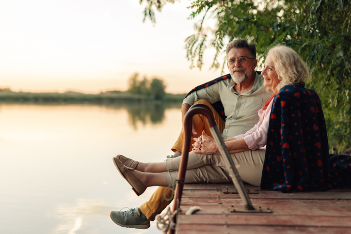 Senior couple relaxing on a pier, sharing a blanket and enjoying the sunset over the lake