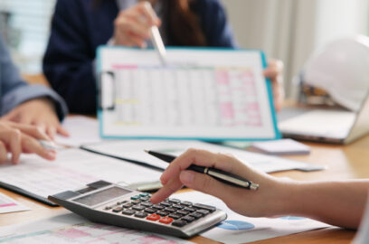 Closeup of conference table; people reviewing numbers in business meeting, financial tables and charts spread across conference table