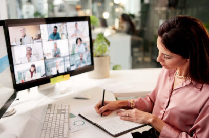 Woman sitting at desk attending online webinar on computer and taking notes in notebook