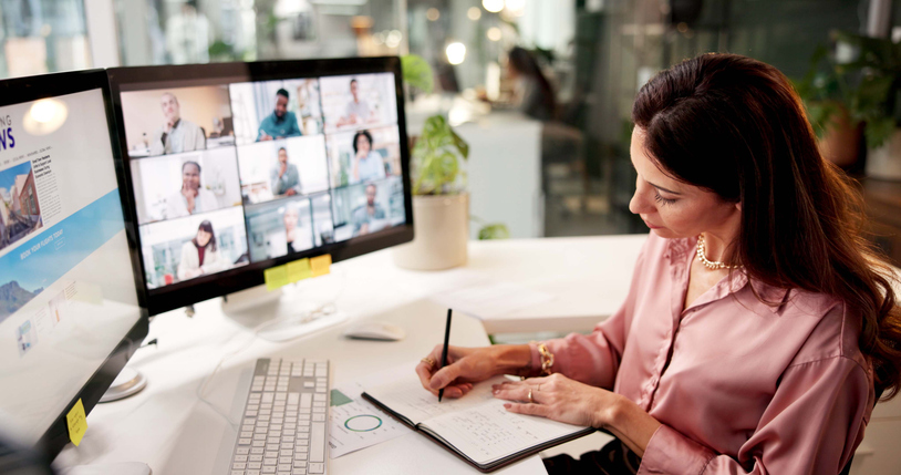 Woman sitting at desk attending online webinar on computer and taking notes in notebook