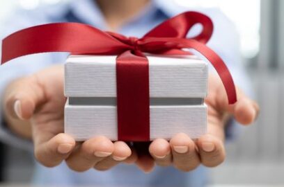 Charitable giving, gifting, hands holding small white box, red ribbon tied in bow