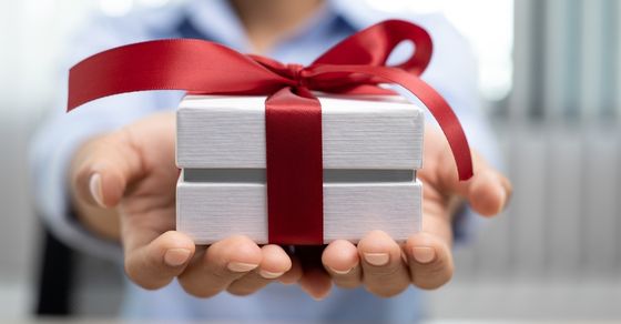 Charitable giving, gifting, hands holding small white box, red ribbon tied in bow