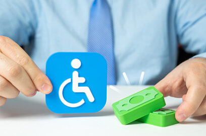 Person holding a disability accessibility symbol beside stacks of money, representing the financial and tax implications of disability benefits.