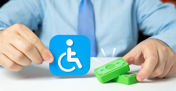 Person holding a disability accessibility symbol beside stacks of money, representing the financial and tax implications of disability benefits.