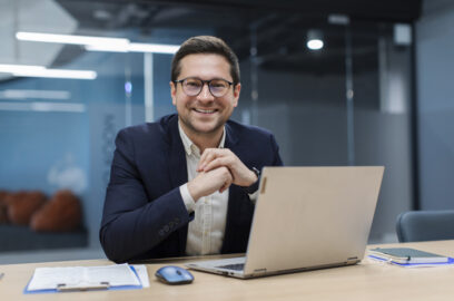 Business professional sitting at desk in front of laptop smiling at camera