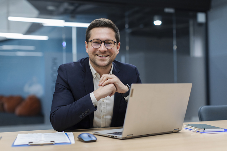 Business professional sitting at desk in front of laptop smiling at camera
