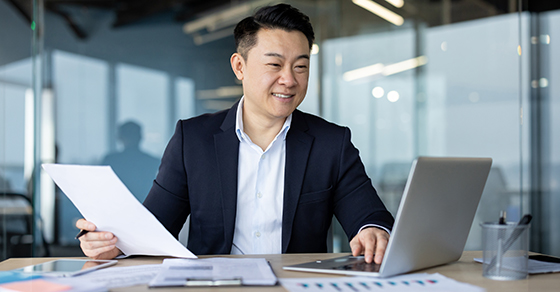 Office setting, man, reviewing documents, checking laptop, reviewing stock, before, year-end